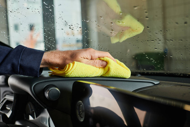 vista cortada de serviceman profissional dedicado usando pano amarelo para limpar carro moderno na garagem - Foto, Imagem
