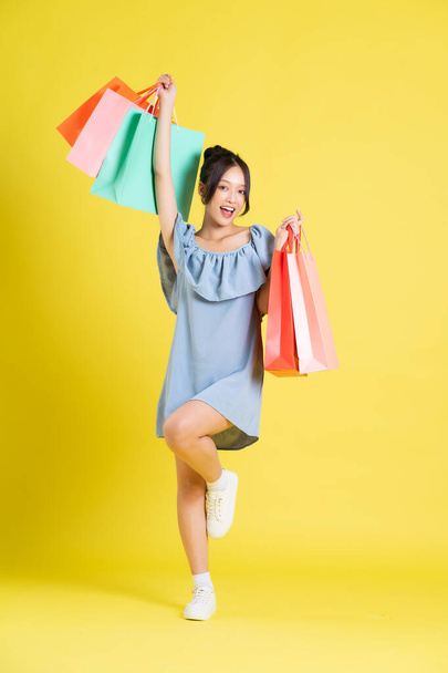 kép egy gyönyörű ázsiai lány egy ruha kezében egy bevásárló táska a kezében pózol egy sárga háttér - Fotó, kép