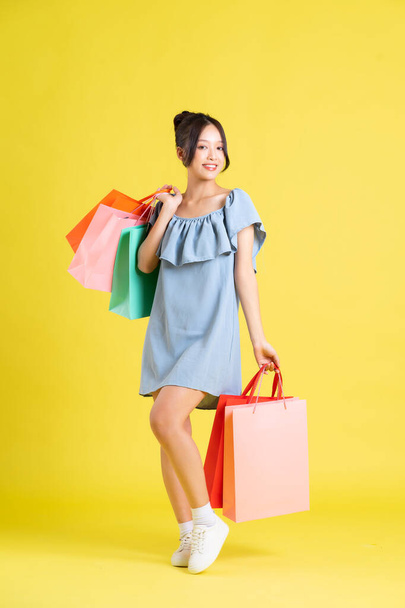 imagem de uma bela menina asiática em um vestido segurando um saco de compras em sua mão posando em um fundo amarelo - Foto, Imagem