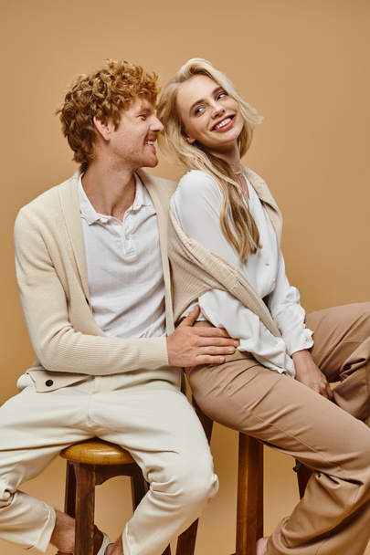 giovane e sorridente coppia in abbigliamento casual alla moda seduto su sedie su grigio, vecchio stile moda soldi - Foto, immagini