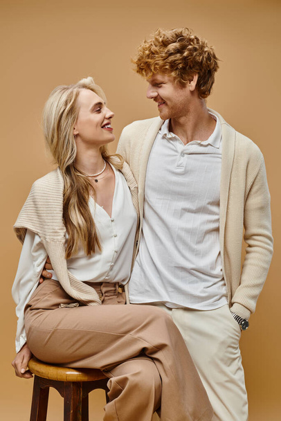 елегантна блондинка і рудий чоловік посміхаються один одному на бежевому тлі, старий стиль моди - Фото, зображення