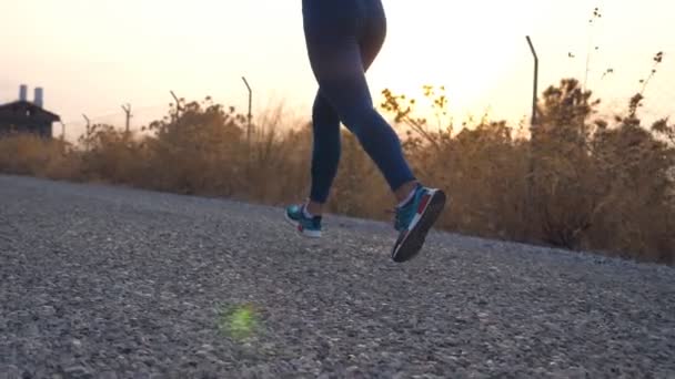 Volg de voeten van een jong meisje dat op de landweg rent. Vrouwelijke benen joggen in de natuur. Sportieve actieve levensstijl. Langzame beweging Lage kijkhoek. - Video