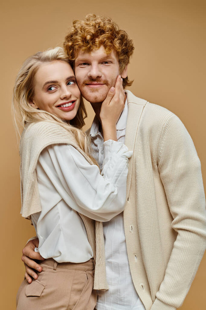 fashionable couple in trendy old money style attire smiling and embracing on grey backdrop - Photo, Image