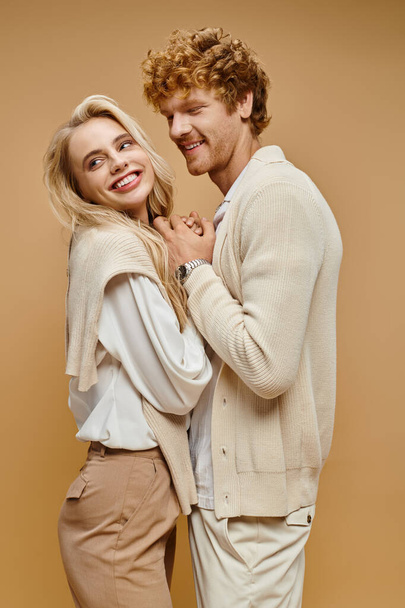 cheerful young couple in trendy old money style outfit holding hands on beige, timeless fashion - Photo, Image