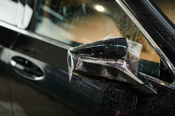 foto objeto de película protetora aplicada cuidadosamente no espelho de visão lateral do carro moderno preto - Foto, Imagem