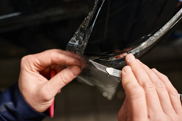 visão recortada do trabalhador profissional que trabalha duro que aplica a folha protetora no carro preto na garagem - Foto, Imagem