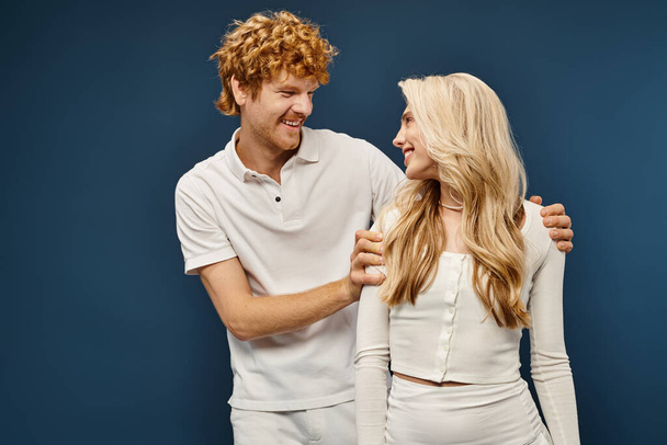 glückliches und wohlhabendes Paar im weißen Outfit, das sich auf blauer, alter Geld-Mode anschaut - Foto, Bild