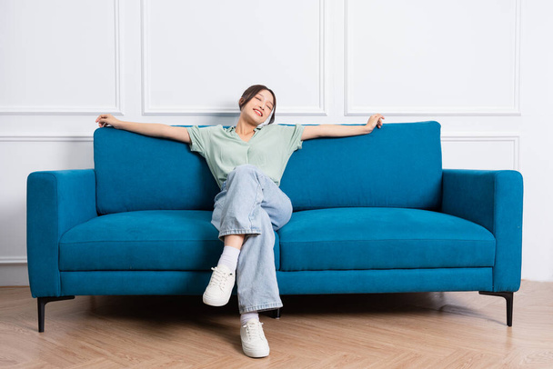 изображение молодой азиатской девушки, сидящей дома на диване - Фото, изображение