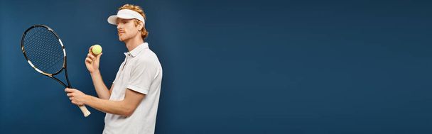 πλούσιος κοκκινομάλλης με λευκό ντύσιμο και αντηλιακό κρατώντας ρακέτα και μπάλα του τένις σε μπλε, πανό - Φωτογραφία, εικόνα