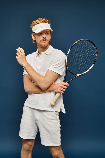 punapää mies valkoisessa puvussa ja aurinko visiiri tilalla maila ja tennis pallo katsellen pois sininen - Valokuva, kuva