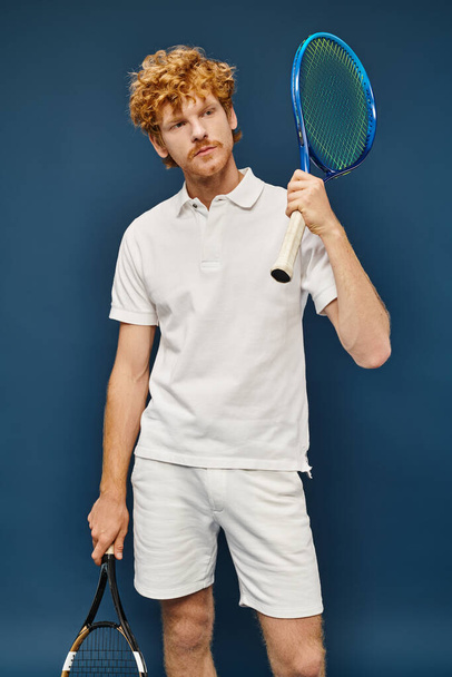 komea punapää mies valkoisessa puvussa tennismailat katselee pois sininen, aktiivinen elämäntapa - Valokuva, kuva