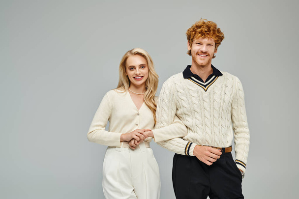 cheerful blonde woman and redhead man in fashionable casual attire looking at camera on grey - Photo, Image