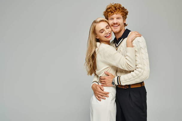счастливая и модная молодая пара в стильной повседневной одежде, обнимающая серую, классическую вневременную моду - Фото, изображение