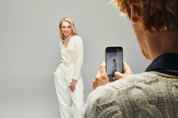 young man taking photo of fashionable blonde woman on grey backdrop, classic fashion concept - 写真・画像
