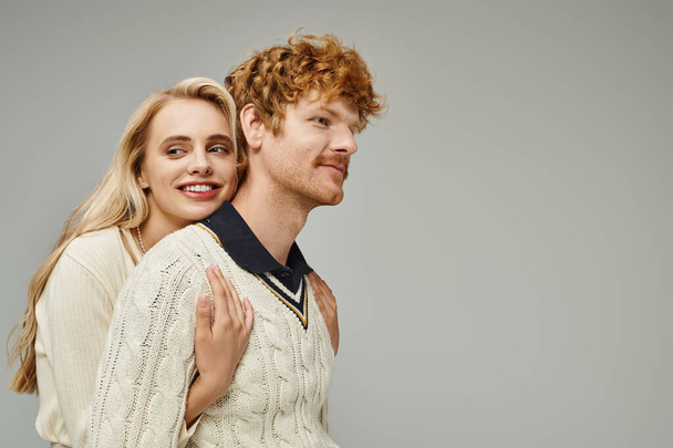 jolly blonde woman embracing young redhead man in stylish casual clothes on grey, timeless fashion - Photo, Image