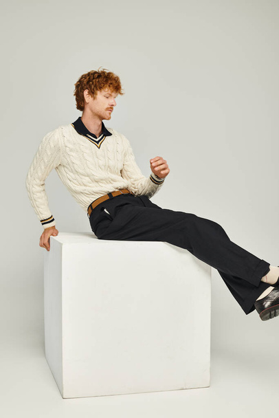 グレー,古いお金スタイルの概念の上に白い立方体に座っているファッショナブルな服の若い赤毛の男 - 写真・画像