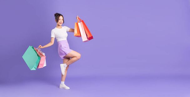 Młoda Azjatka trzyma torbę na zakupy na fioletowym tle - Zdjęcie, obraz