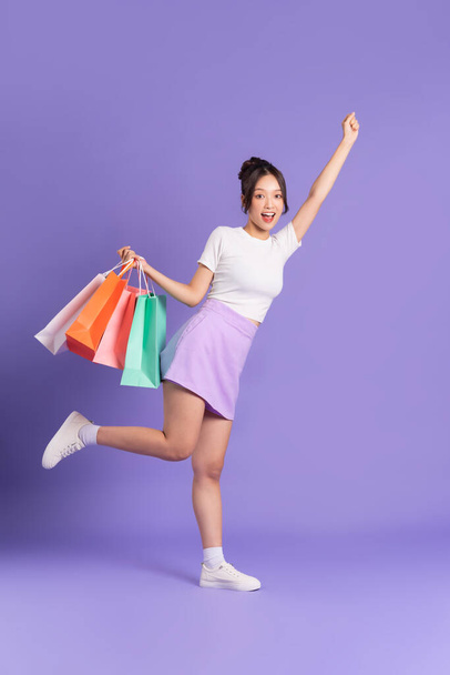 Молодая азиатка держит сумку для покупок на фиолетовом фоне - Фото, изображение