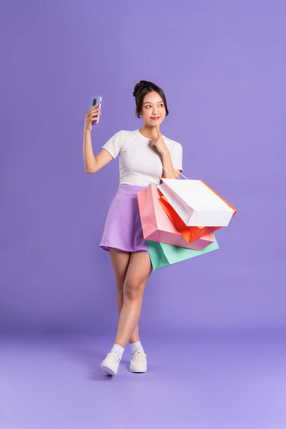 Jeune femme asiatique tenant sac à provisions sur fond violet - Photo, image