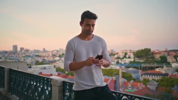 Handsome guy making call at evening cityscape. Athletic brunette waiting date speaking mobile phone on city park terrace. Urban latino man typing smartphone having cellphone conversation on street. - Footage, Video