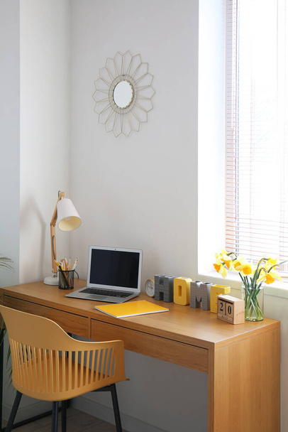 Komfortabler Arbeitsplatz mit modernem Laptop und Narzissenblumen auf dem Tisch im Zimmer - Foto, Bild