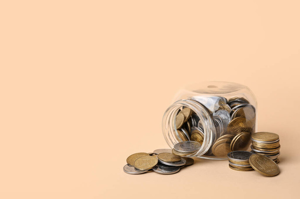 Overturned jar with coins on beige background. Savings concept - Photo, Image