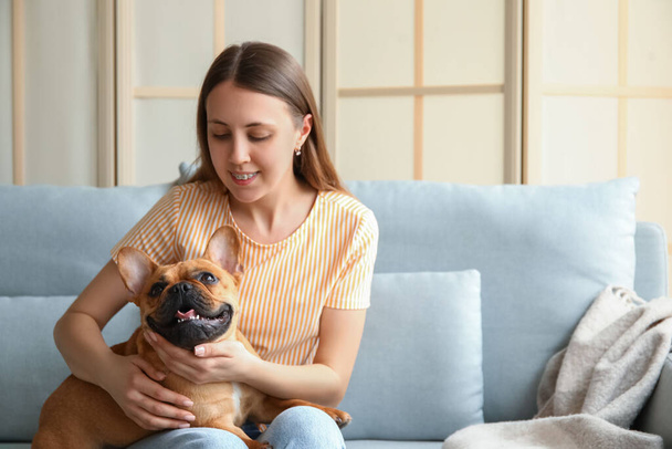 Young woman with cute French bulldog sitting on sofa at home - Photo, Image