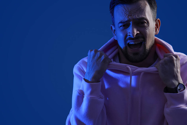 Young man having panic attack on blue background, closeup - Photo, Image