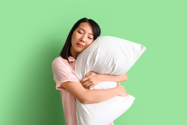 Beautiful Asian woman in pajamas with pillow on green background - Photo, Image