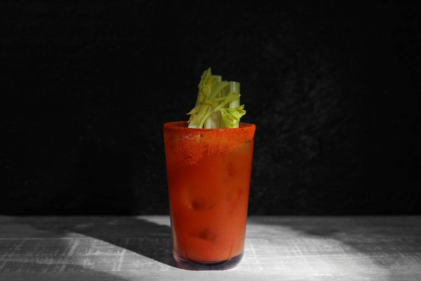 Glas Bloody Mary met selderij op houten tafel tegen donkergroene achtergrond - Foto, afbeelding