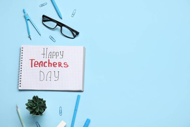 Notebook s textem HAPPY TEACHERS DAY, brýle a kancelářské potřeby na modrém pozadí - Fotografie, Obrázek