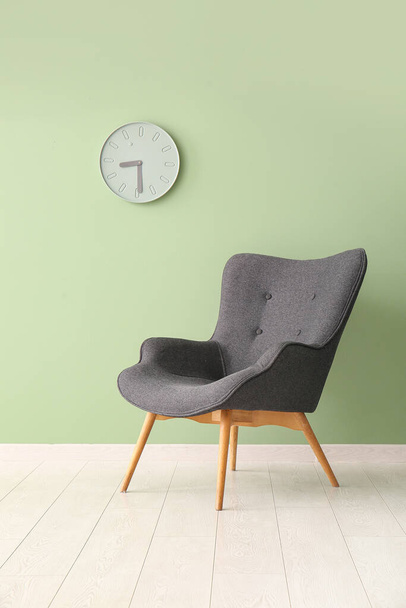 Сіре крісло і годинник біля зеленої стіни - Фото, зображення