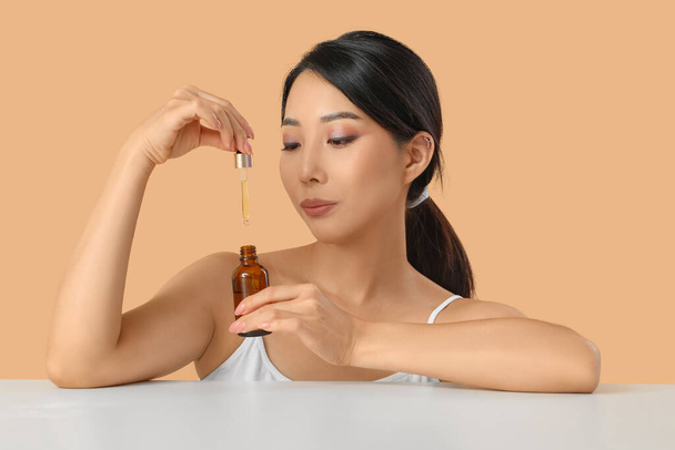 Hermosa mujer asiática joven con aceite cosmético sobre fondo beige - Foto, Imagen