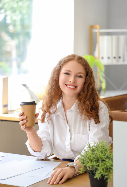 Joven empresaria con taza de café sentada en la oficina - Foto, Imagen