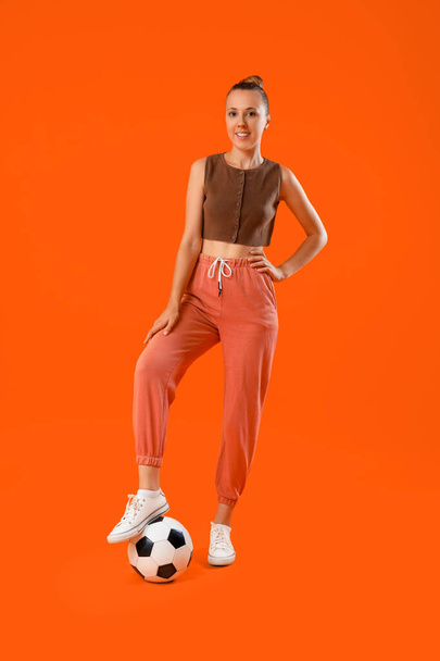 Krásná mladá sportovní žena s fotbalovým míčem na oranžovém pozadí - Fotografie, Obrázek