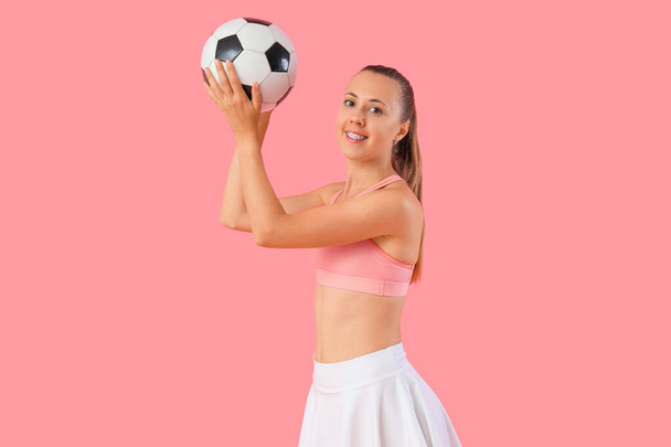 Happy beautiful young sporty woman with soccer ball on pink background - Photo, Image
