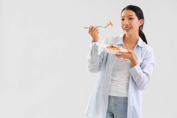 Young Asian woman eating tasty pasta on light background - Photo, Image
