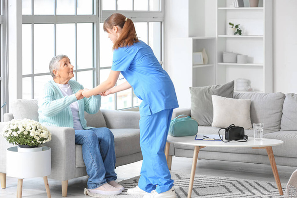 Jonge verzorger helpt oudere vrouw om thuis op te staan - Foto, afbeelding
