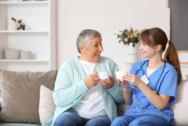 Senior woman with caregiver drinking coffee at home - Photo, Image