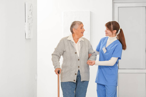 Femme âgée avec bâton de marche et soignant dans le couloir - Photo, image
