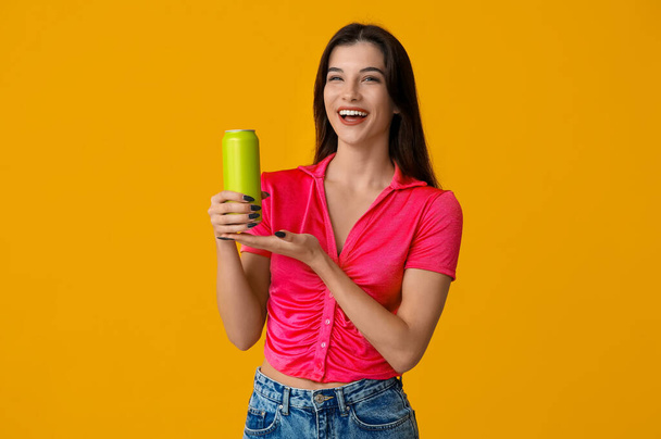 Beautiful young woman with can of cold beer on yellow background - Photo, Image
