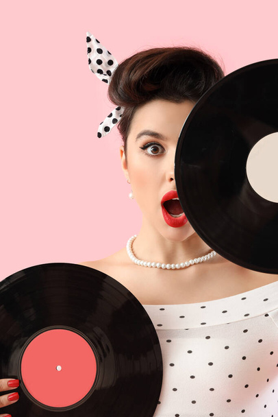 Šokovaný mladý pin-up žena s vinyl disky na růžovém pozadí, detailní záběr - Fotografie, Obrázek