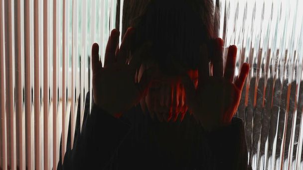 Депрессивный ребенок, прислонившись к стеклянному окну, чувствует печаль и отчаяние, борясь с психическими заболеваниями в детстве - Фото, изображение