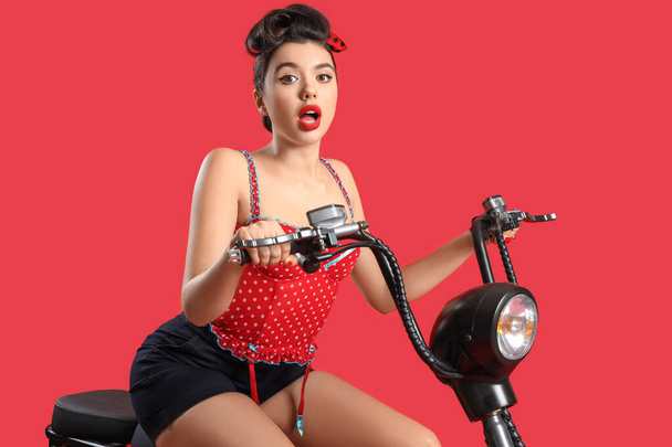 Attractive young pin-up woman riding bike on red background - Photo, Image