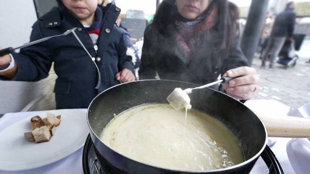 Mother and Child Enjoying Swiss Fondue on Vacation, close-up of hot traditional European food at restaurant during cold winter season - Photo, Image