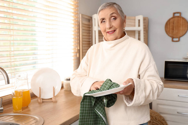 Mujer mayor que limpia la placa en la cocina - Foto, imagen