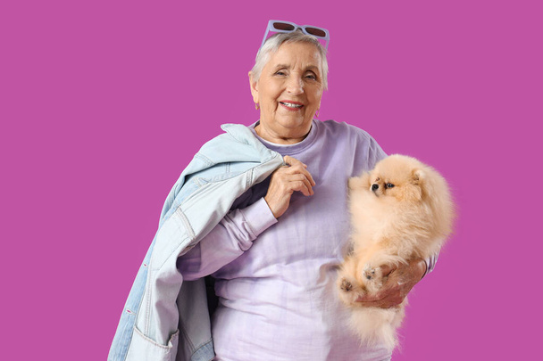 Senior vrouw met Pomeranian hond op paarse achtergrond - Foto, afbeelding