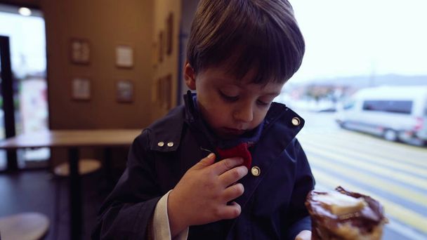 Bambino accidentalmente macchia sciarpa con cono gelato mentre mangia trattare in salotto, indossando giacca. Madre regola i vestiti del figlio per proteggere dalla macchia - Foto, immagini