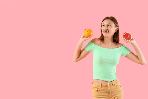 Hübsche junge Frau mit Zitrusfrüchten auf rosa Hintergrund - Foto, Bild
