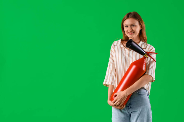 Portrait of young woman with fire extinguisher on green background - Foto, Imagem